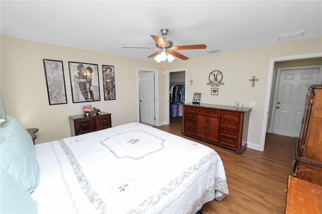 bedroom with a spacious closet, visible vents, baseboards, and wood finished floors