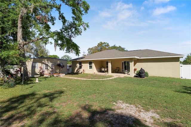 rear view of house featuring stucco siding, an outbuilding, a yard, and fence