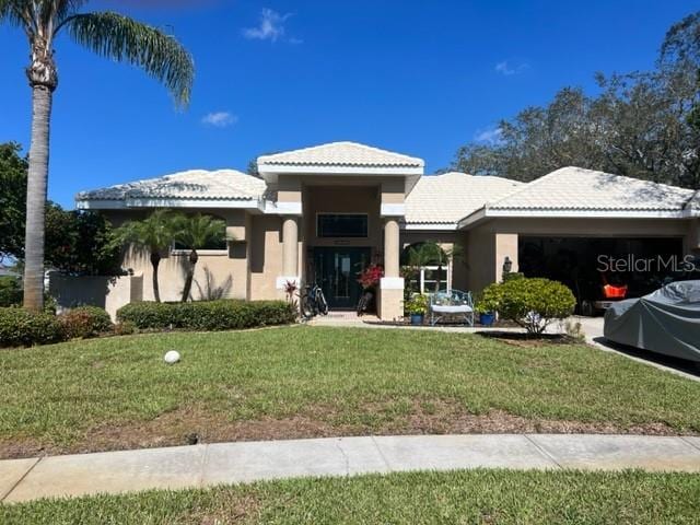 view of front facade with a front lawn, a tiled roof, a garage, and stucco siding