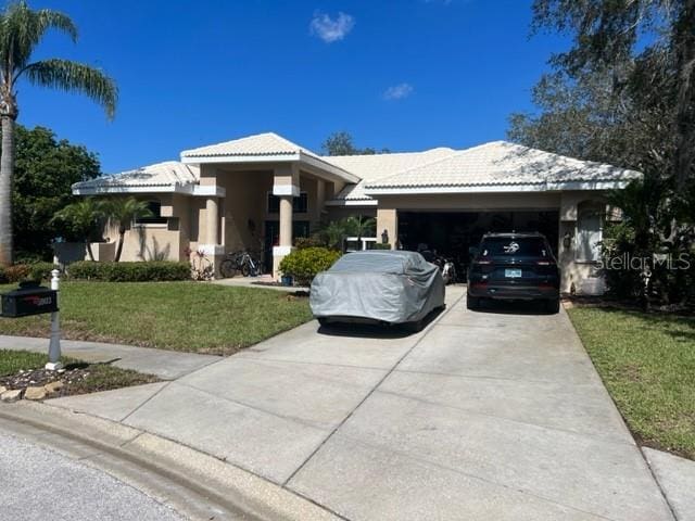 view of front of home with a tiled roof, a front yard, stucco siding, a garage, and driveway