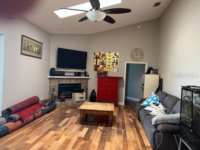 living area with visible vents, a ceiling fan, wood finished floors, vaulted ceiling with skylight, and a fireplace