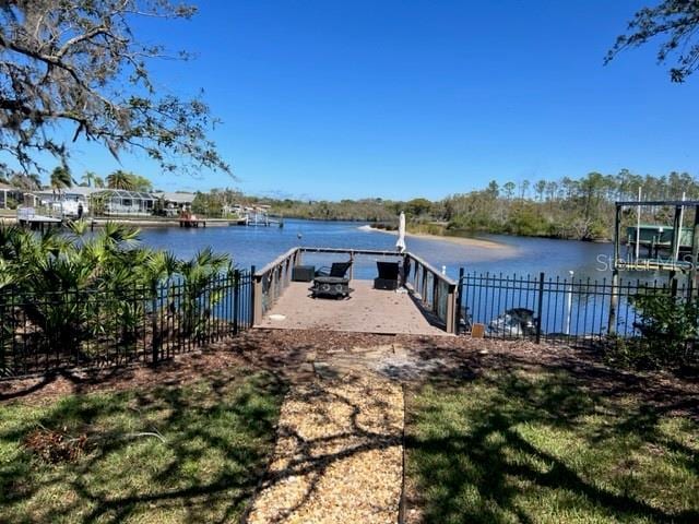 dock area with fence, a water view, and a lawn