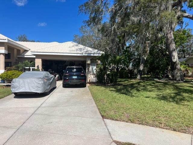 view of side of property with driveway, a yard, stucco siding, a garage, and a tiled roof