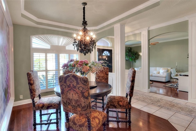 dining space with ornamental molding, ceiling fan with notable chandelier, a tray ceiling, arched walkways, and tile patterned flooring