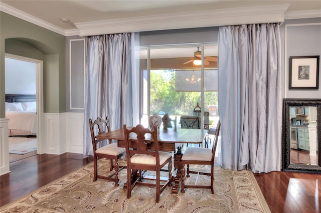 dining area with wainscoting, wood finished floors, ceiling fan, and ornamental molding