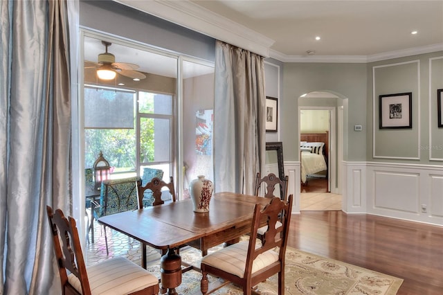 dining space with a wainscoted wall, wood finished floors, arched walkways, crown molding, and a decorative wall