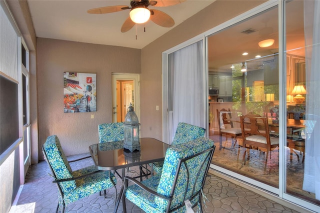 dining area with a textured wall, visible vents, ceiling fan, and a sunroom