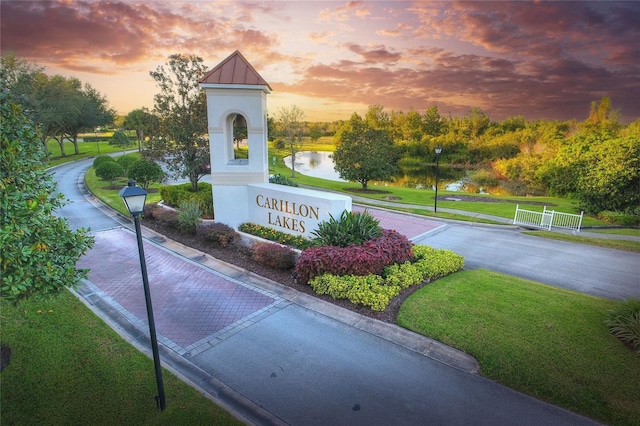 community sign featuring driveway, a yard, and a water view