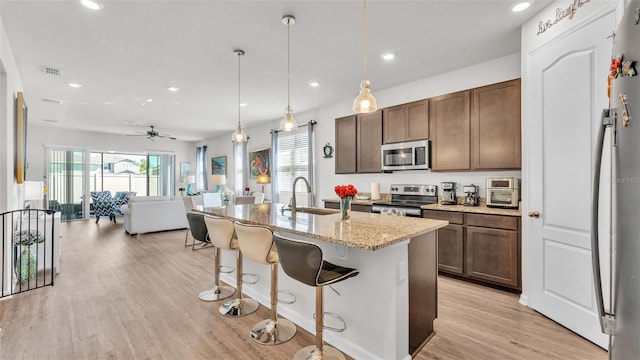 kitchen with light stone countertops, a breakfast bar, a sink, light wood-style floors, and appliances with stainless steel finishes