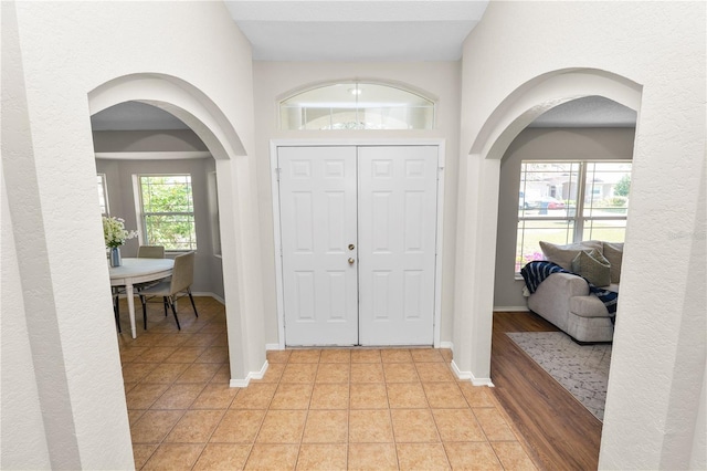 foyer entrance featuring light tile patterned floors, baseboards, and arched walkways