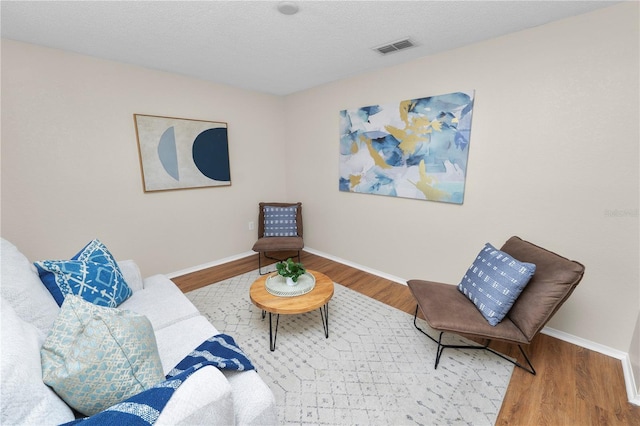 sitting room featuring visible vents, a textured ceiling, baseboards, and wood finished floors