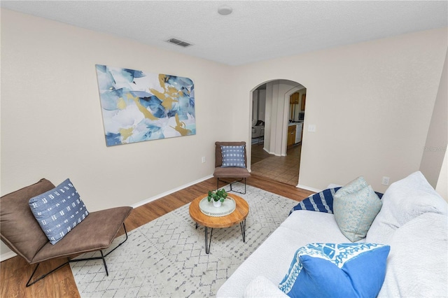 living area featuring visible vents, baseboards, wood finished floors, arched walkways, and a textured ceiling