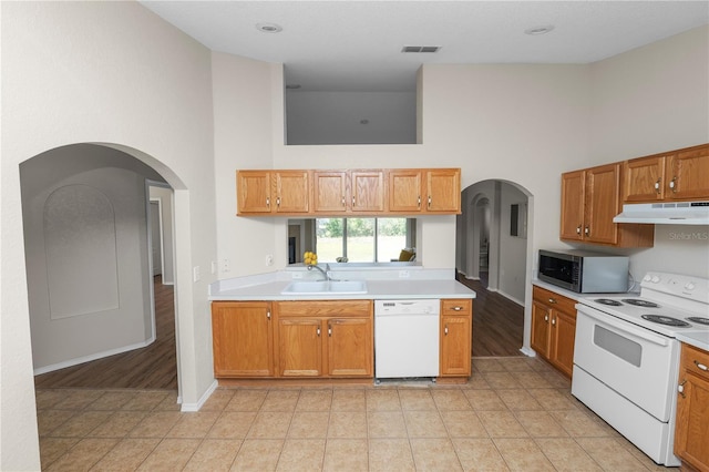 kitchen featuring a sink, white appliances, under cabinet range hood, and a towering ceiling