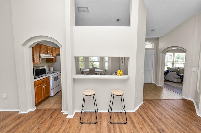 kitchen with a kitchen bar, visible vents, white electric range, stainless steel microwave, and brown cabinetry