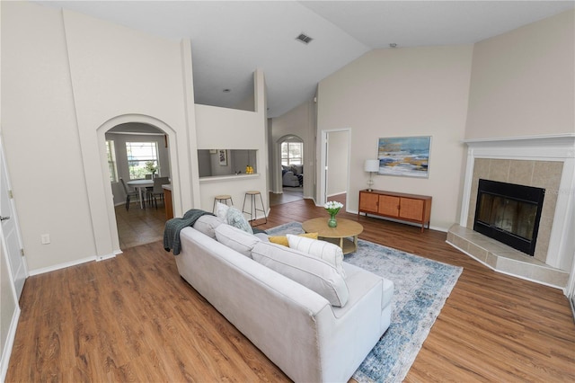 living room with visible vents, a fireplace, wood finished floors, arched walkways, and high vaulted ceiling