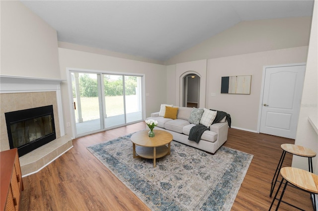 living room featuring a tiled fireplace, lofted ceiling, and wood finished floors