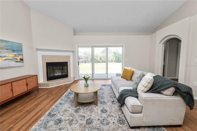 living room with arched walkways, a tile fireplace, wood finished floors, and vaulted ceiling