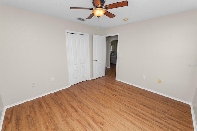 unfurnished bedroom featuring visible vents, a closet, arched walkways, light wood-style floors, and baseboards