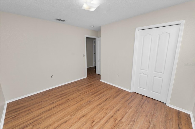 unfurnished bedroom with visible vents, light wood-style flooring, a textured ceiling, and baseboards