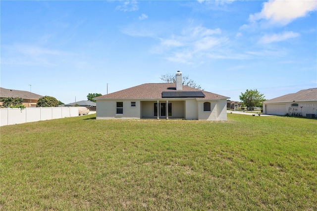 rear view of house with roof mounted solar panels, a chimney, a yard, and fence