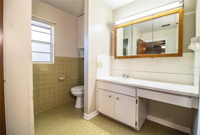 bathroom with toilet, vanity, wainscoting, tile patterned floors, and tile walls