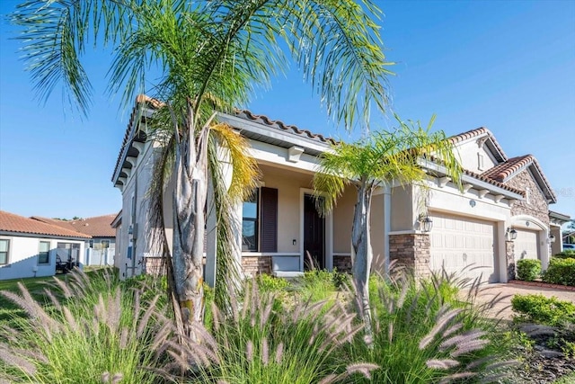 view of front of home featuring a tiled roof, stucco siding, driveway, stone siding, and an attached garage