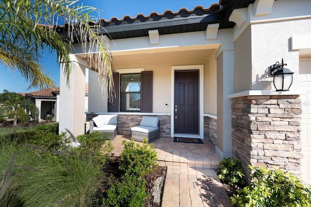 doorway to property featuring stone siding, covered porch, a tiled roof, and stucco siding