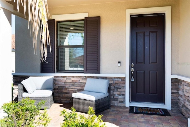 entrance to property featuring stucco siding, stone siding, and covered porch