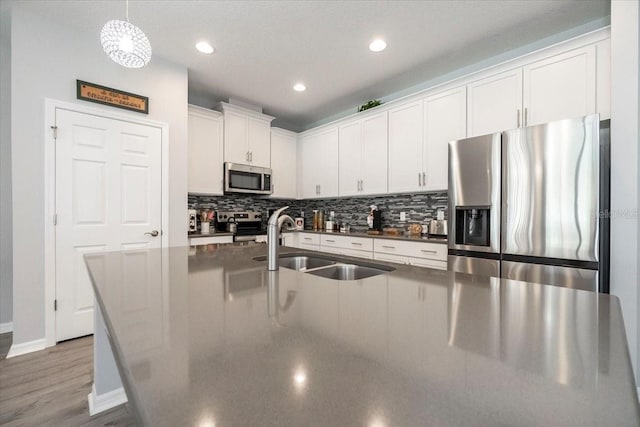 kitchen featuring a sink, stainless steel appliances, white cabinetry, dark countertops, and backsplash