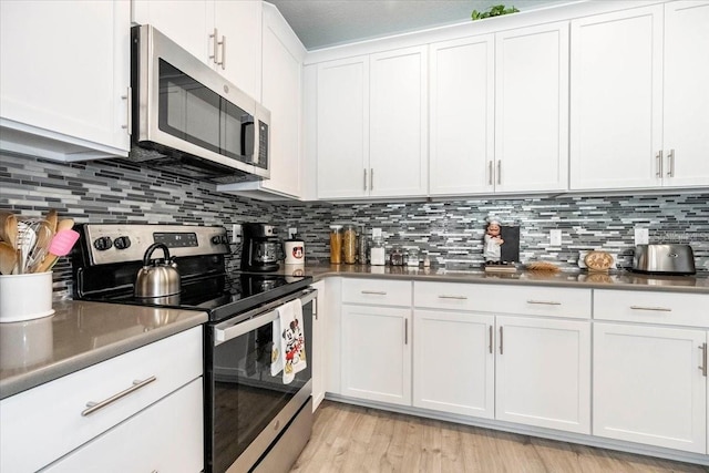 kitchen with light wood-style floors, appliances with stainless steel finishes, white cabinetry, dark countertops, and backsplash