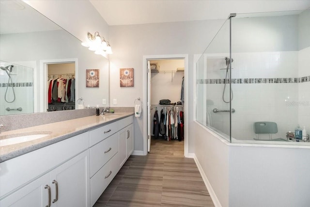 full bathroom with double vanity, a walk in shower, a walk in closet, and a sink