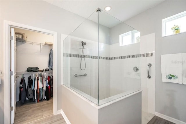 bathroom with a walk in shower, a walk in closet, baseboards, and wood finished floors