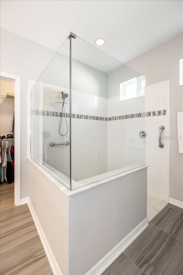 bathroom with a spacious closet, baseboards, walk in shower, and wood finished floors