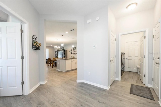 corridor with a chandelier, visible vents, baseboards, and light wood-style floors