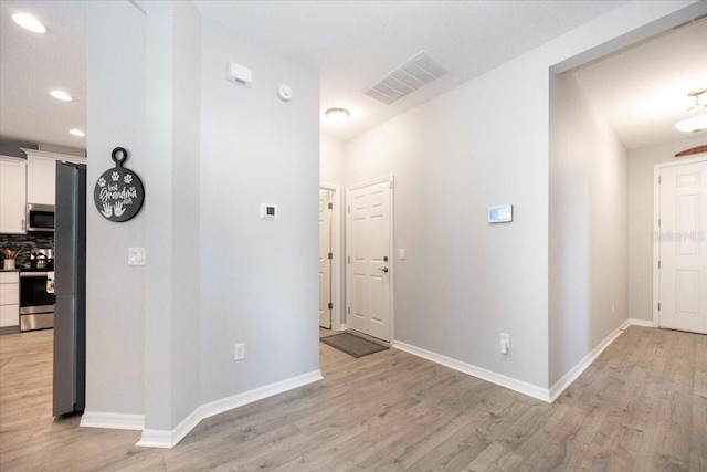 hallway featuring baseboards, visible vents, and light wood finished floors