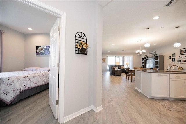 kitchen featuring open floor plan, light wood-style flooring, hanging light fixtures, white cabinetry, and a sink