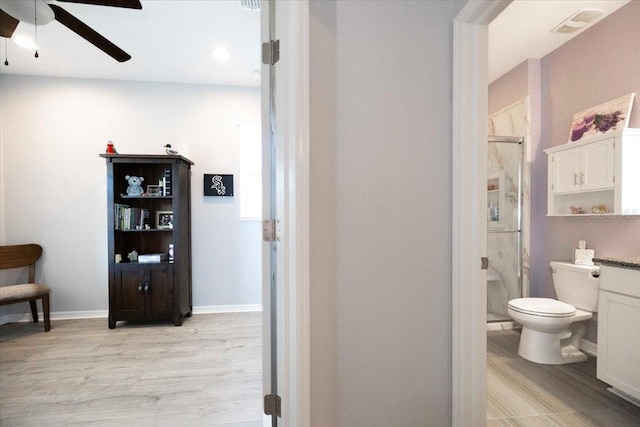 bathroom with baseboards, ceiling fan, toilet, a stall shower, and wood finished floors