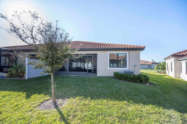 rear view of house featuring a tiled roof, a yard, a sunroom, and stucco siding