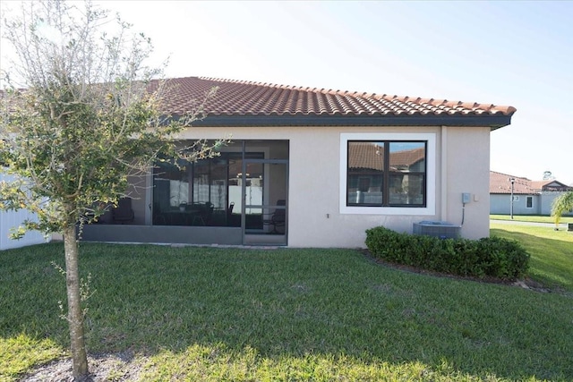 back of house with stucco siding, a tile roof, a yard, and a sunroom