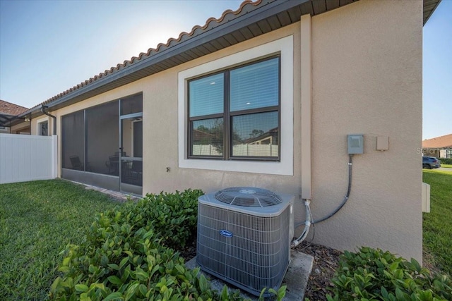 view of side of home with a tile roof, central AC unit, a lawn, stucco siding, and a sunroom