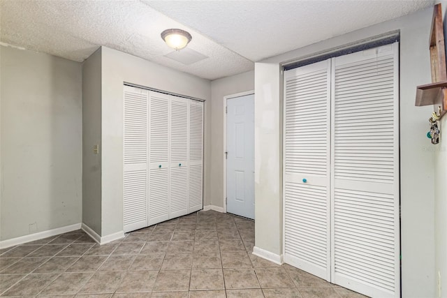 unfurnished bedroom with light tile patterned flooring, baseboards, two closets, and a textured ceiling