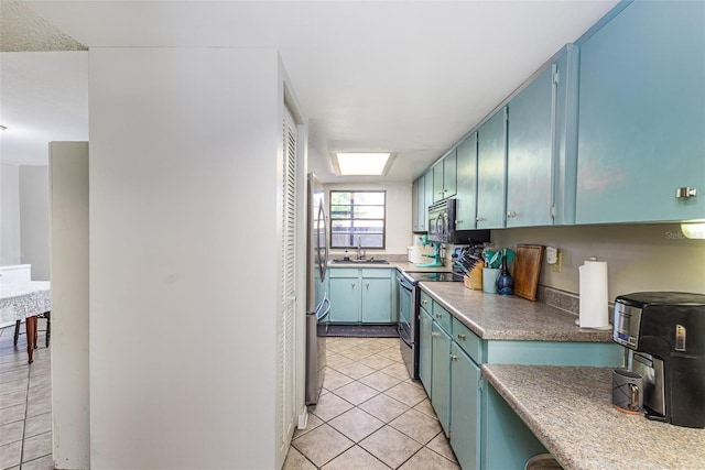 kitchen featuring blue cabinetry, light tile patterned flooring, appliances with stainless steel finishes, and a sink