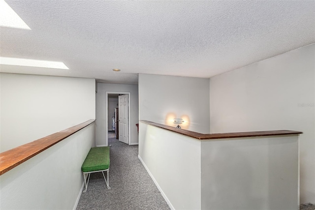 hall featuring carpet flooring, an upstairs landing, baseboards, and a textured ceiling