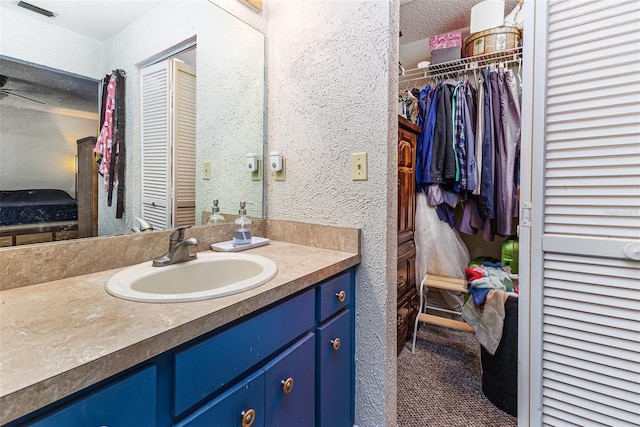 bathroom featuring vanity, visible vents, a spacious closet, a textured ceiling, and a textured wall