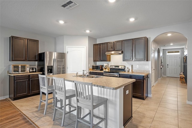 kitchen with visible vents, arched walkways, a sink, under cabinet range hood, and appliances with stainless steel finishes