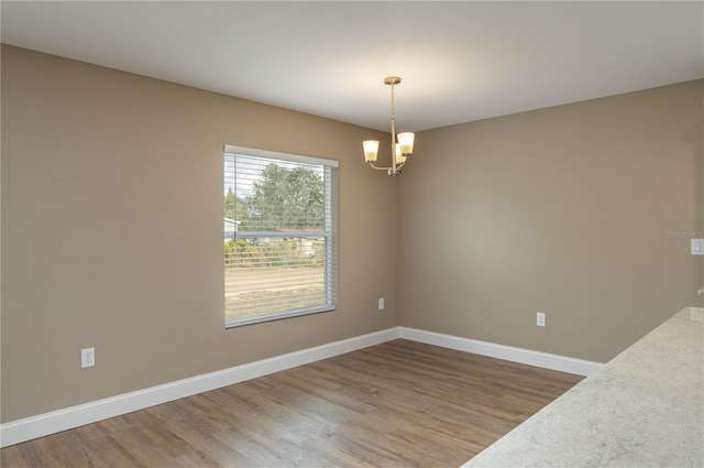 empty room with a chandelier, baseboards, and wood finished floors