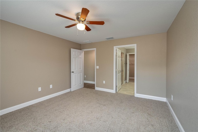 unfurnished bedroom featuring visible vents, light carpet, a walk in closet, baseboards, and ceiling fan