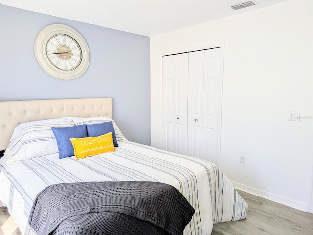 bedroom with a closet, visible vents, baseboards, and wood finished floors