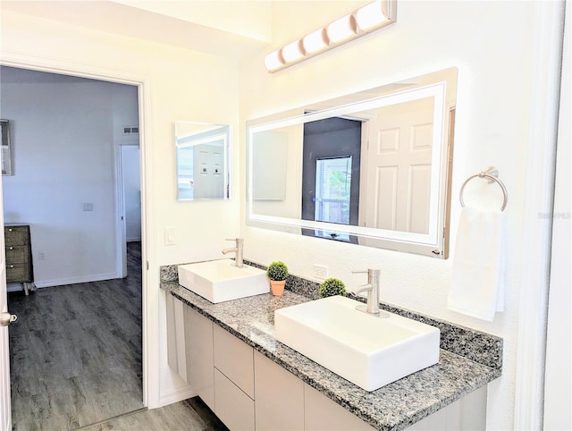 full bath with double vanity, wood finished floors, baseboards, and a sink