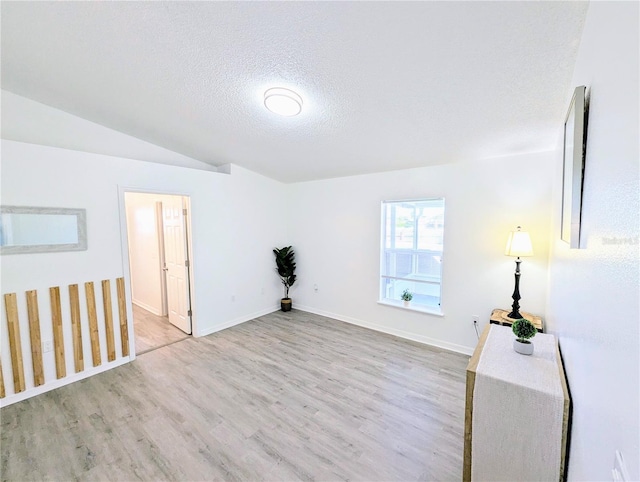 empty room featuring vaulted ceiling, wood finished floors, baseboards, and a textured ceiling